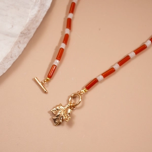 Close-up of beaded necklace with orange and white beads, gold maple leaf pendant and OT clasp