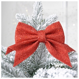 Glittery red Christmas bow hanging on a snowy tree branch with festive bokeh lights