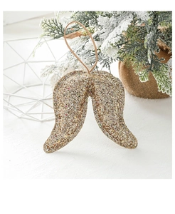 Close-up of golden glittery angel wing ornament beside a mini frosted Christmas tree