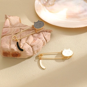 Cute black and white enamel cat safety pin brooches with swaying tails on a stone display