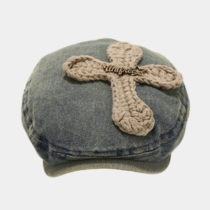 Close-up view of a retro washed denim beret featuring a crocheted cross and star pin.