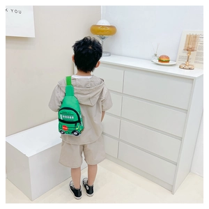 Rear view of a child wearing the green cartoon school bus chest bag in a home setting