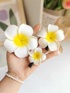 Detailed view of three different sizes of white and yellow frangipani flower hair clips