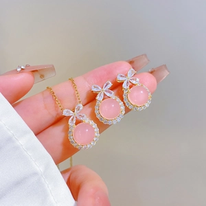 Detail of gold titanium bow necklace and earrings set with pink stones and zircons