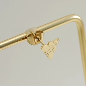 Macro detail of a golden bee-shaped stainless steel stud earring on a display stand