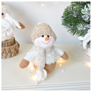 Close-up of a plush knitted snowman doll with warm lights and festive pine branches