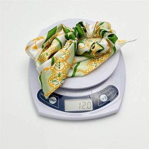Close-up of lightweight satin bow hair tie with green stripes and vintage patterns on a scale