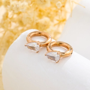 Elegant gold teardrop zircon hoop earrings displayed on a white minimalist platform