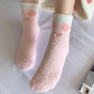 Close-up of fluffy pink coral fleece socks featuring cute pig embroidery and white cuffs