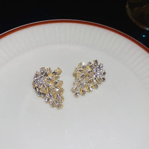 Macro detail of leaf-shaped gold stud earrings with sparkling cubic zirconia on ceramic