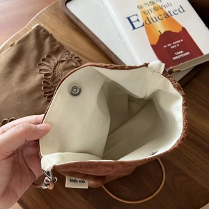 Détail du sac bandoulière en daim camel avec doublure blanche, bouton et étiquette
