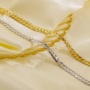 Polished gold and silver snake chain necklaces displayed on elegant satin fabric