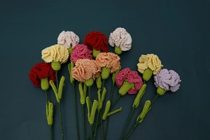 Flat lay of 12 multi-colored hand-crocheted carnations on a deep teal background