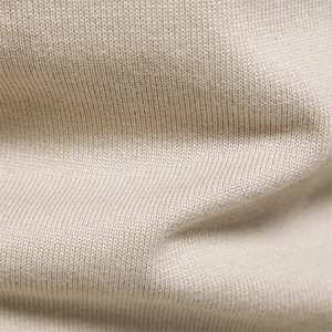 Macro shot of high-quality beige cotton knit fabric showing soft texture and fine grain