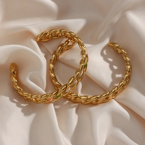 Fashionable golden twisted cable cuff bracelet with woven texture on beige satin backdrop
