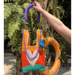 Detail of colorful knit tote bag featuring a white heart pattern and purple chain strap