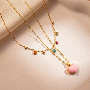 Detail of gold necklace with pink enamel heart and colorful clover charms on a warm background