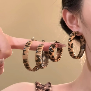 Close-up of leopard print hoop earrings in three sizes on fingers with ear model