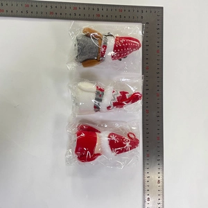 Trois poupées de Noël en peluche tricotée mesurées avec une règle sur un bureau blanc