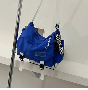 Blue nylon messenger bag featuring white adjustable straps and a checkerboard pendant charm