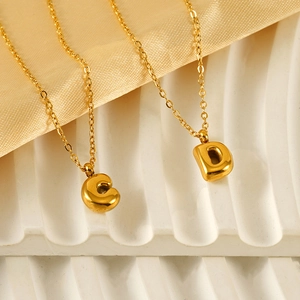 Minimalist 18K gold bubble letter necklaces with C and D pendants on a white textured tray