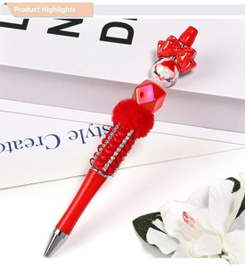 Close-up of decorative red beaded pen with Santa theme and plush ball on a white book