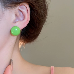 Close-up of bright green ball stud earring worn on ear with minimalist glossy finish