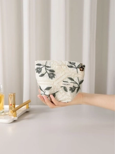 Linen makeup bag with green leaf embroidery and flower pendant held in hand