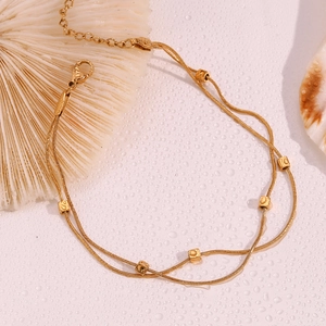 Double-layered 18K gold plated anklet with square beads on a textured surface with shells