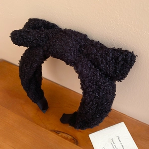 Detailed view of the black plush bow headband with thick lamb wool texture on wood surface