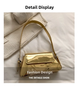 Detailed shot of metallic gold glossy shoulder bag with adjustable strap on white fabric