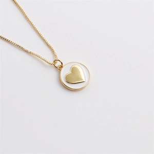 Dettaglio di un ciondolo rotondo placcato oro con cuore in smalto bianco e catena a box