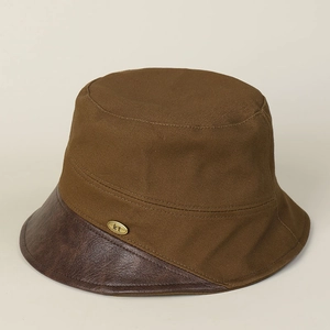 Detail of canvas bucket hat featuring brown leather brim and metal logo ornament