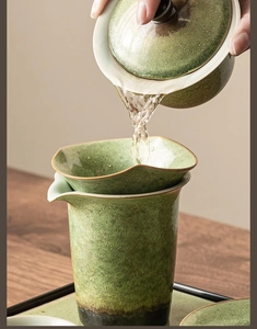 Action shot of pouring tea through a green speckled ceramic tea strainer on wood