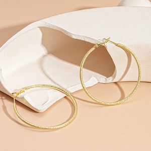 Detail of gold hoop earrings with matte textured finish on a minimalist display