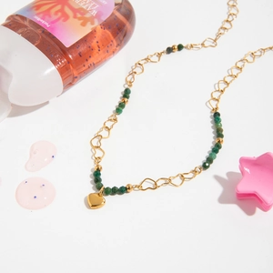 Close-up of golden hollow heart chain links and green faceted natural stone beads