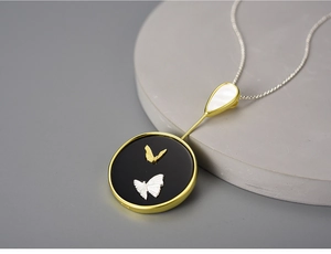 Detail of S925 butterfly pendant with black enamel base and pearl shell on gold chain