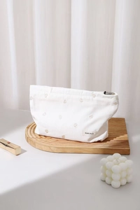 Close-up of heart embroidery on cream striped fabric cosmetic bag with brand label