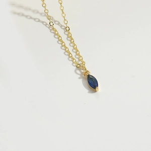 Detailed view of an elliptical blue gemstone pendant on a fine golden necklace chain