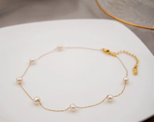 Detail of a vintage pearl anklet with gold chain and lobster clasp on a white plate