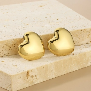 Macro shot of gold heart-shaped stud earrings with smooth finish on beige stone