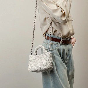 White hand-woven leather bucket bag with metal chain strap shown on a model