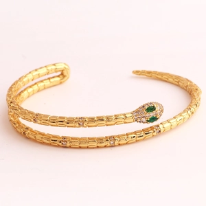 Detailed close-up of golden snake bracelet with green gem eyes and white crystal inlay