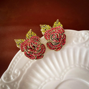 Macro shot of luxury rose-shaped earrings with red rhinestones on a ceramic plate