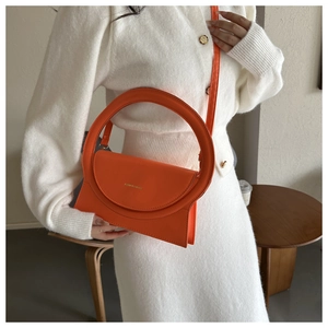 Detail einer leuchtend orangefarbenen Handtasche mit runder Metallgriff und Goldprägung