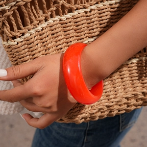 Close-up of chunky orange resin bangle with high gloss finish on woman's wrist