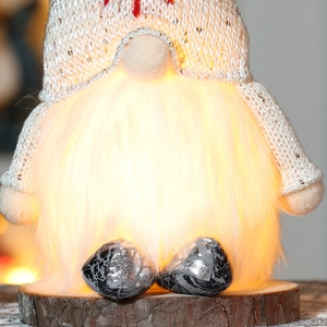 Close-up of a lit Christmas gnome with knit texture, faux fur and a natural wooden base