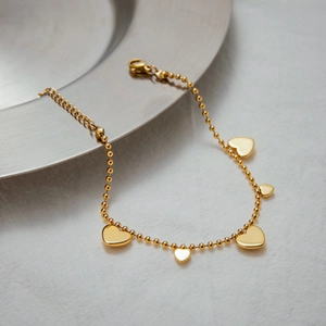 Close-up of gold 18k plated beaded heart bracelet with five heart pendants on metal tray