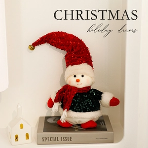 Plush Christmas snowman figurine with red sequined hat on books in festive interior