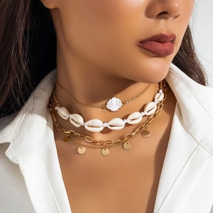 Detail of layered gold pendant necklace set with white shell charm on model